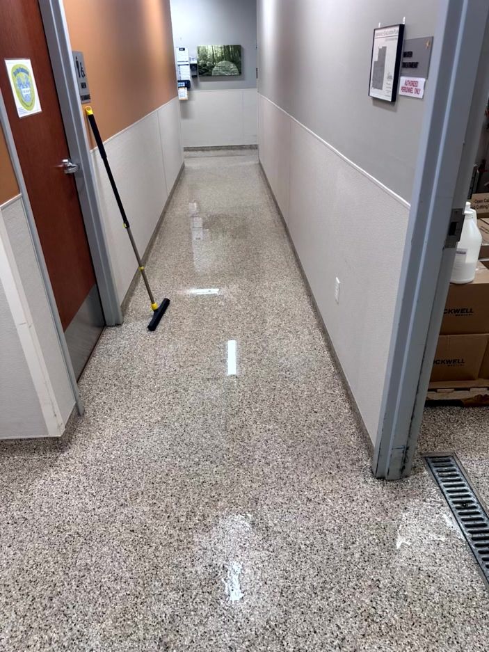 A hallway with a wet, reflective floor and a cleaning squeegee leaning against the left wall.