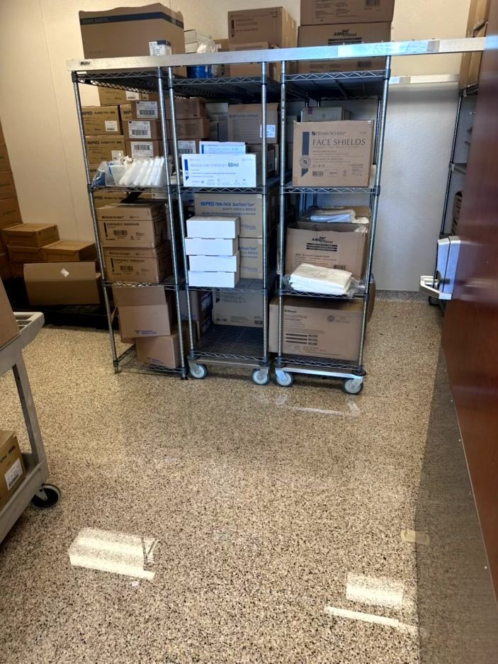 Metal storage racks holding various boxes and supplies in a room with a speckled floor.