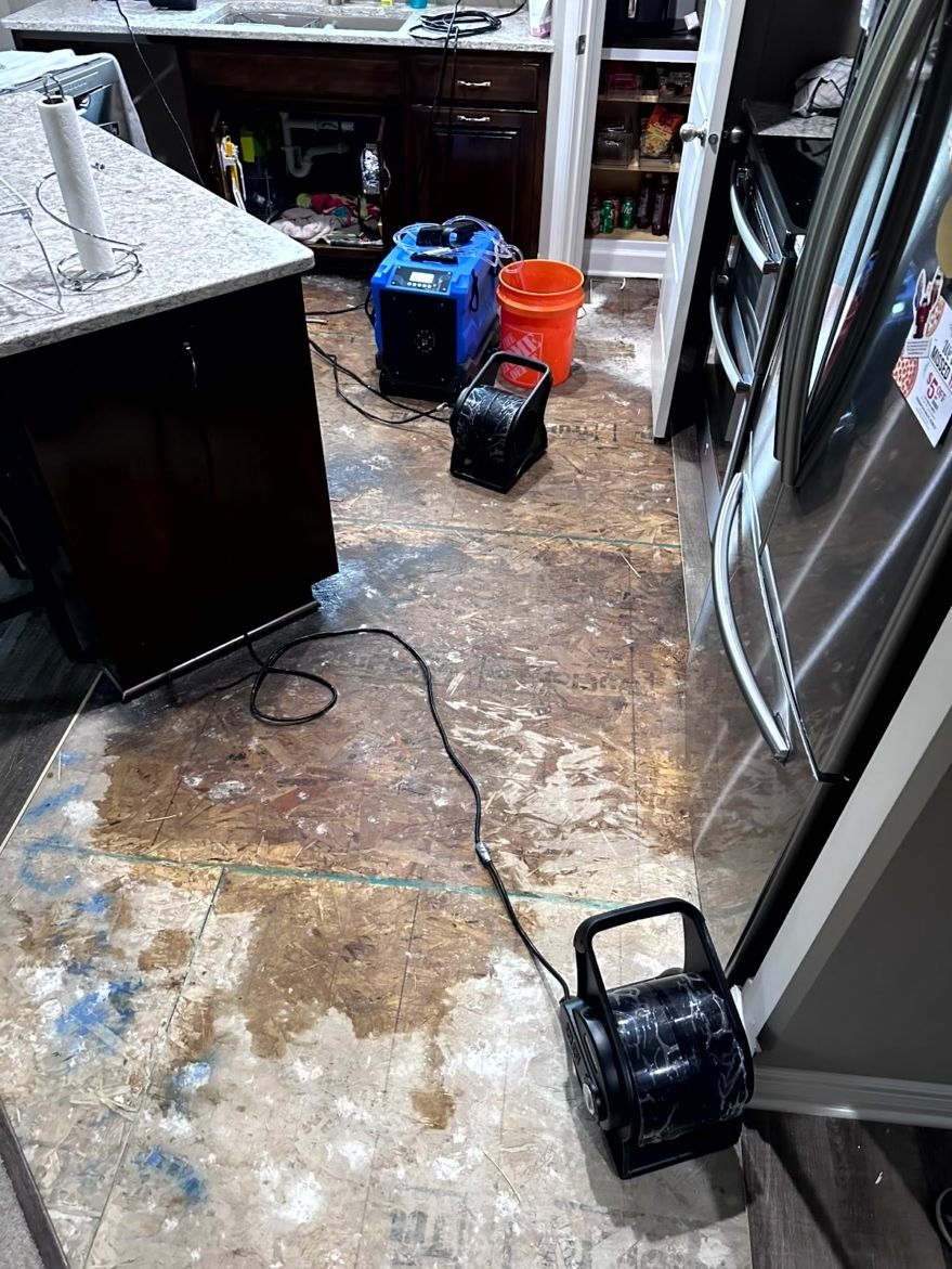 Drying equipment, including fans and a dehumidifier, sits on a subfloor in a kitchen undergoing water damage restoration.