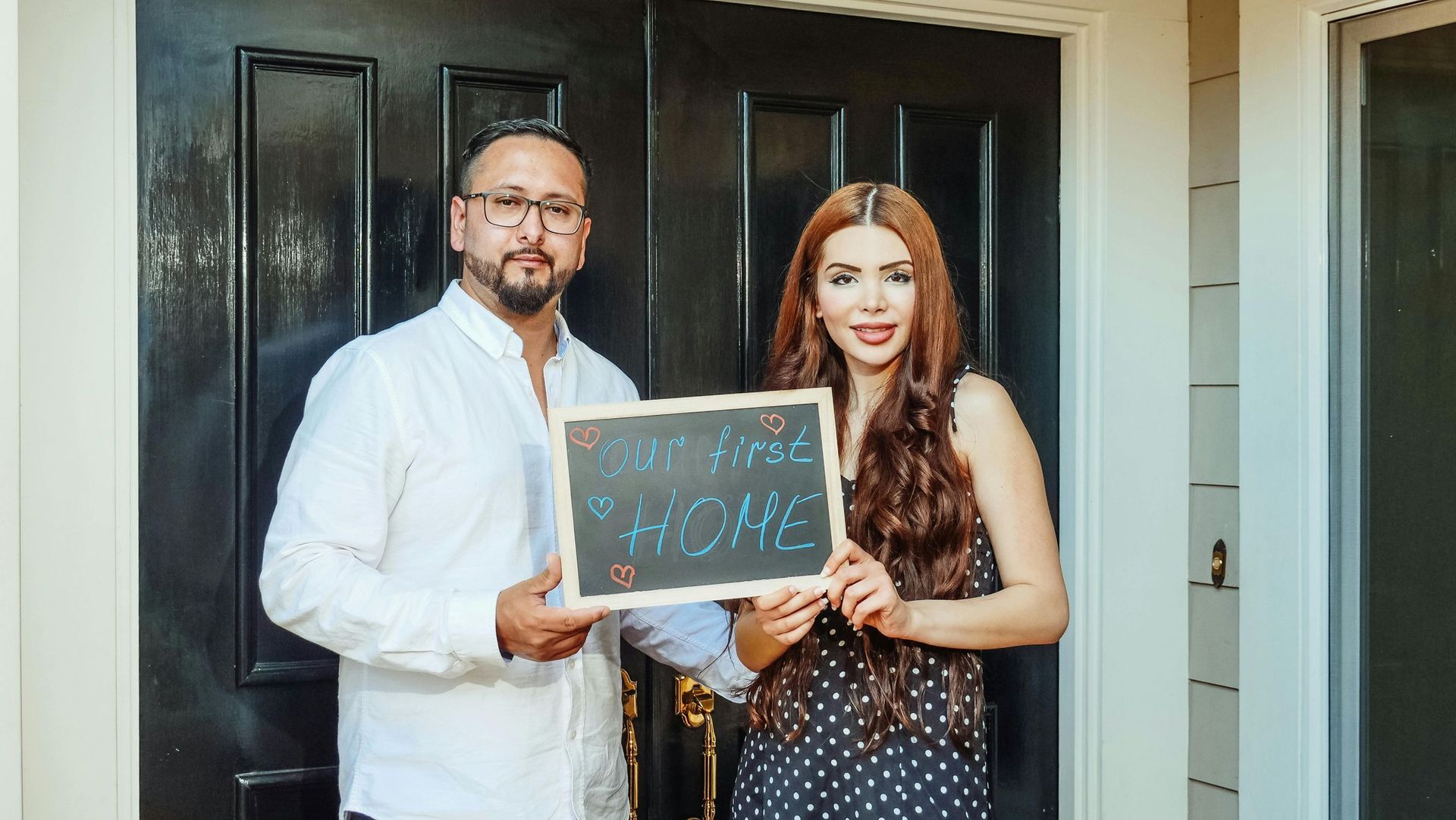 couple holding chalkboard in front house