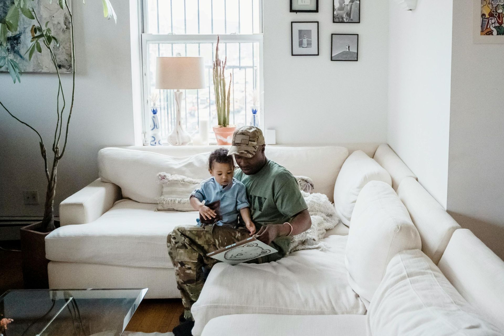 Military man is sitting on a couch with a baby boy on his lap.