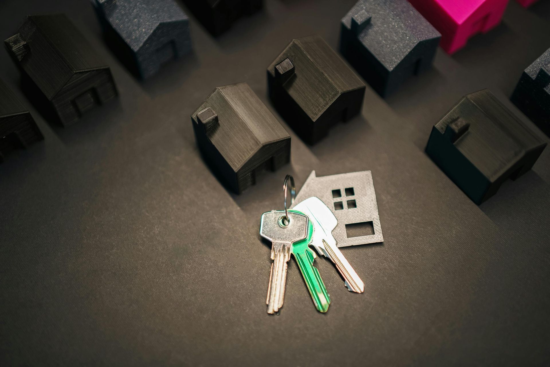 Keys with green keychain on a dark tabletop beside small black house models and a silver key card
