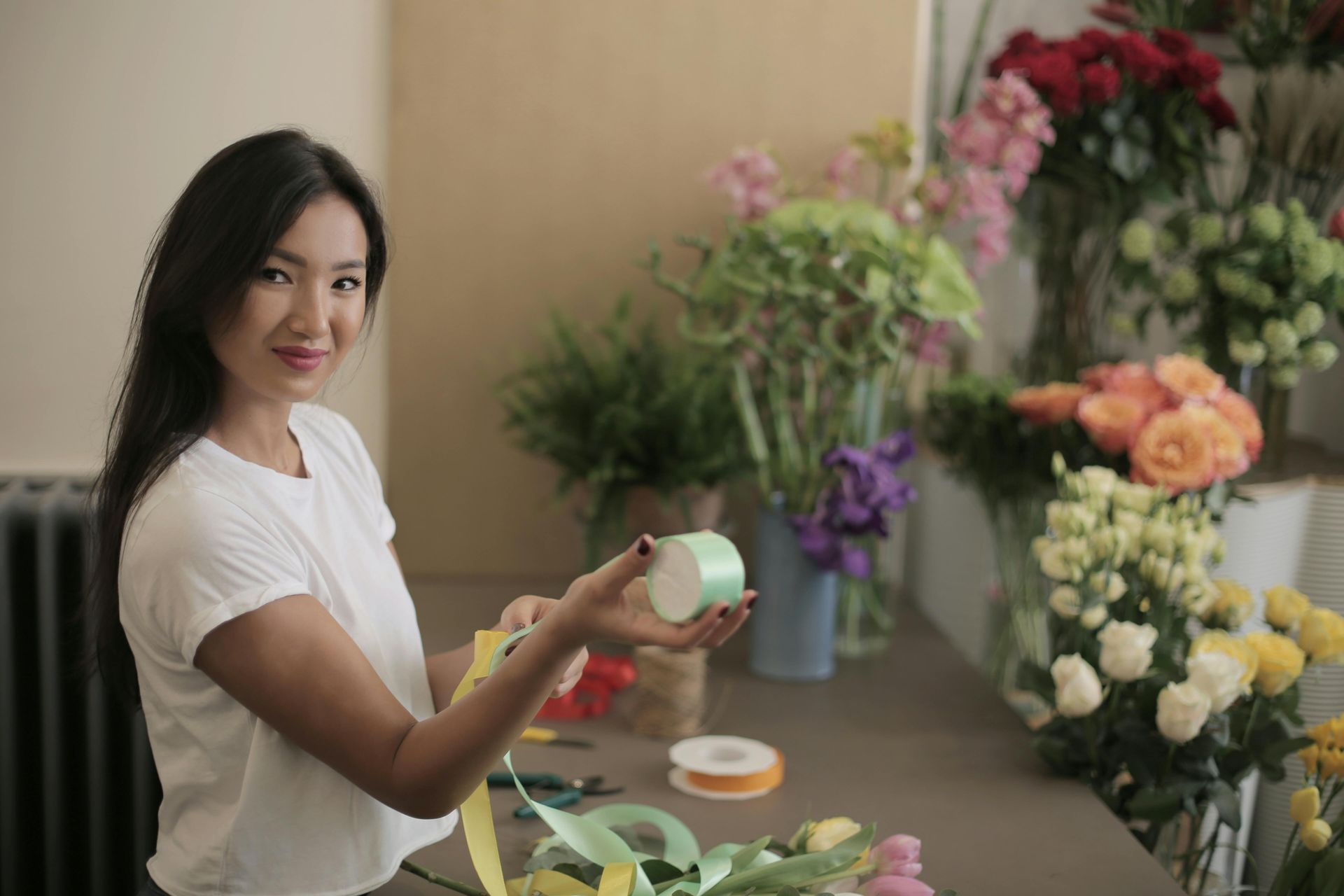 Woman (sole traders home loans wollonong) arranging flowers, holding ribbon in a florist shop.