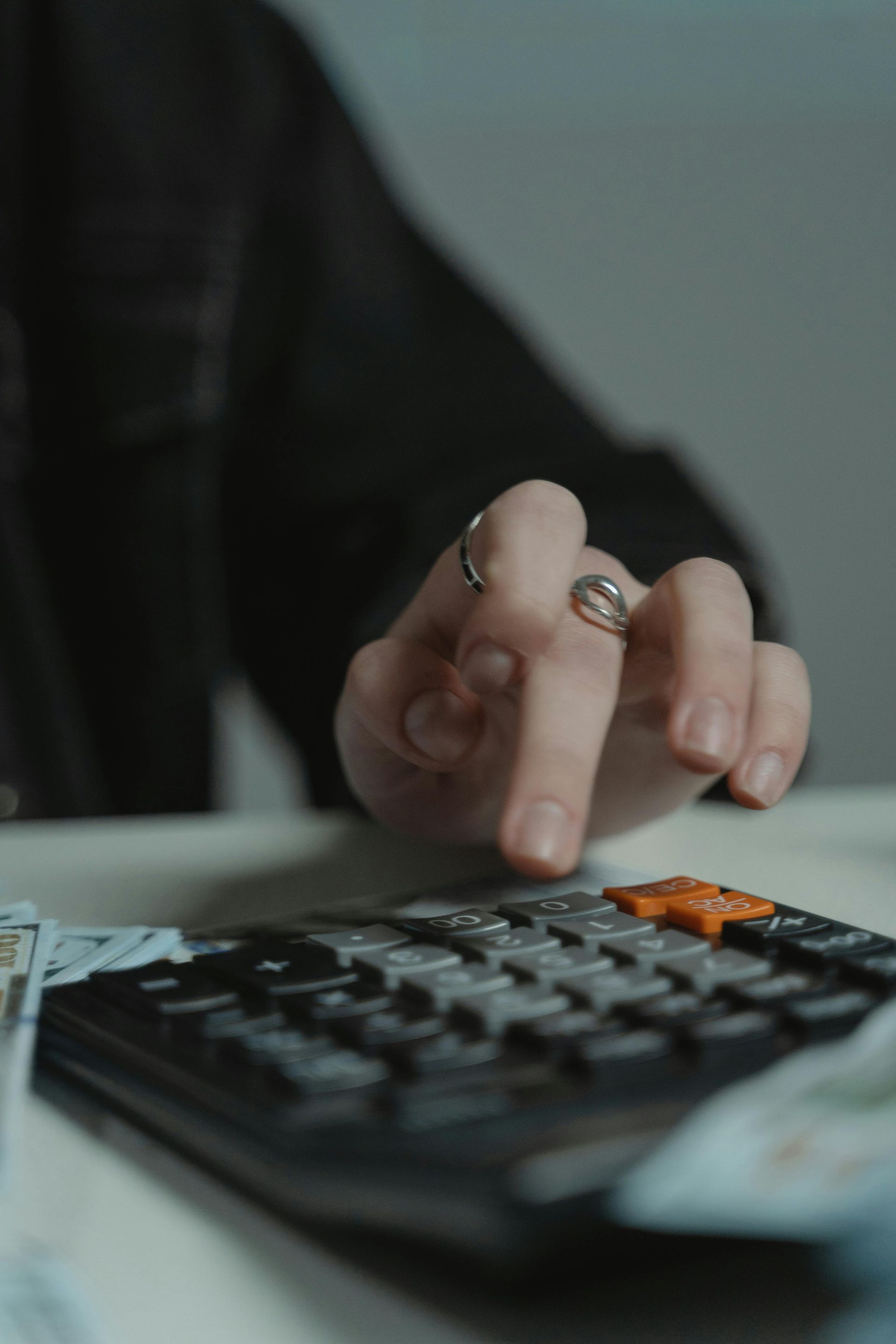 Hand pressing buttons on a calculator beside a white pen on a desk