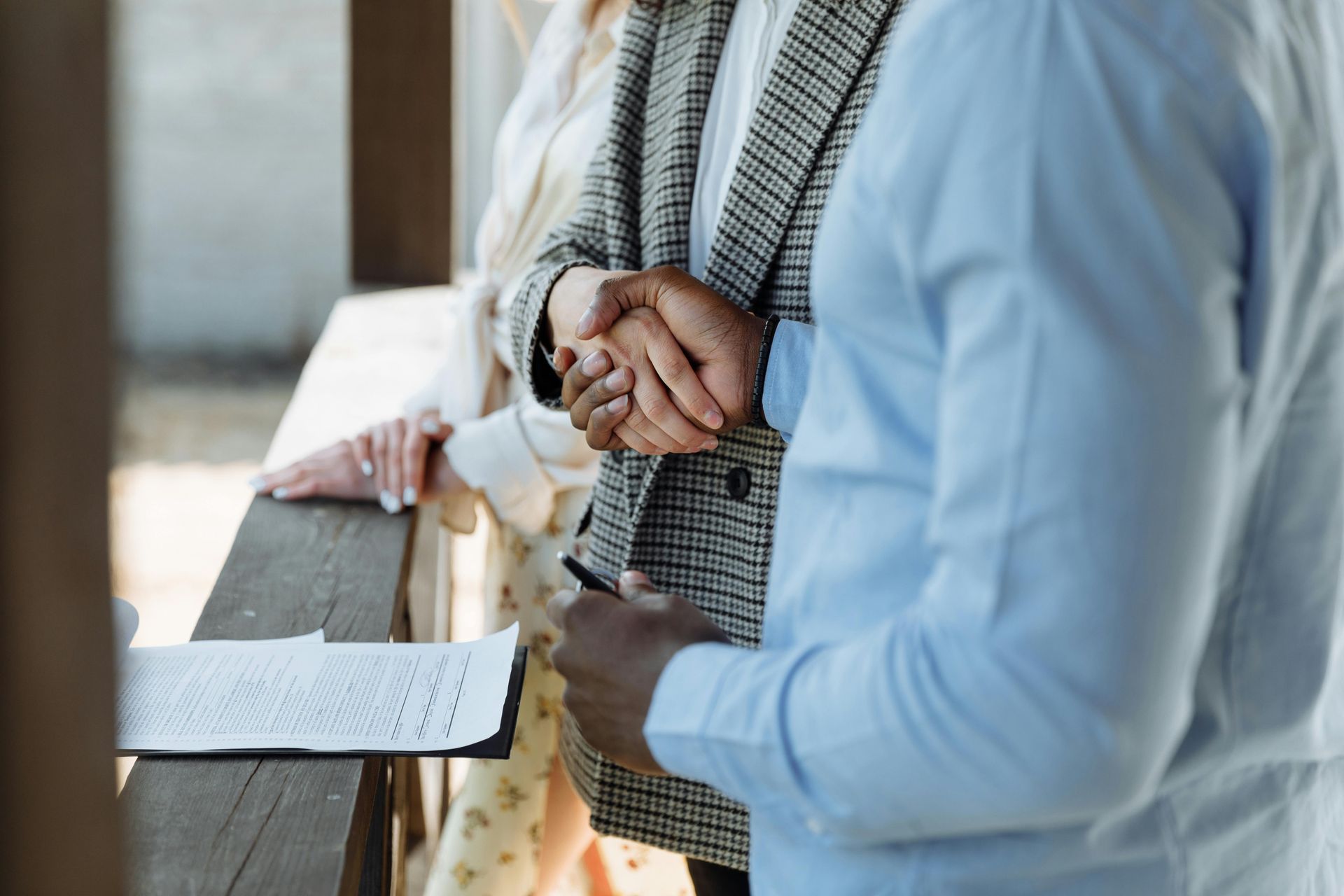 Two people shake hands over a document resting on a wooden railing.