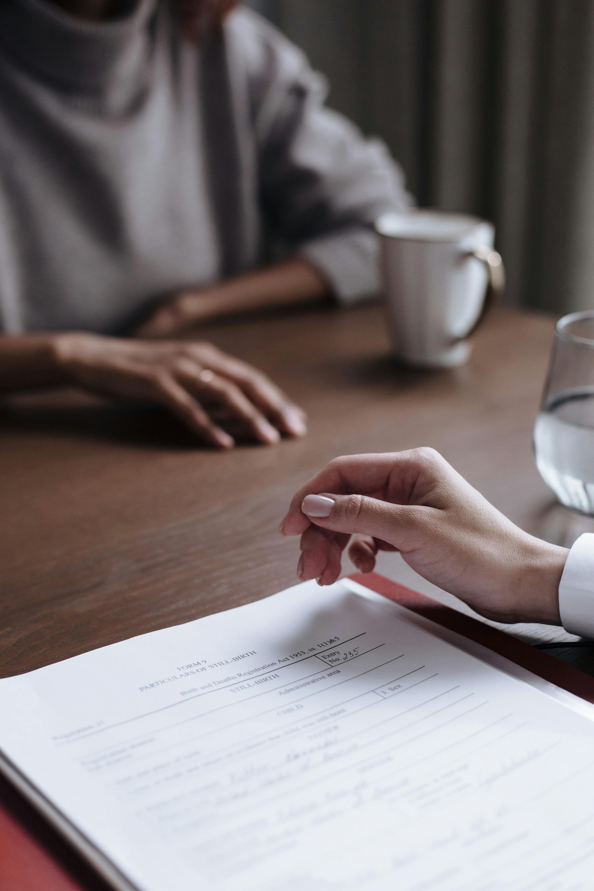 Hands over a document on a wooden table with a coffee mug and glass in a soft-lit meeting setting