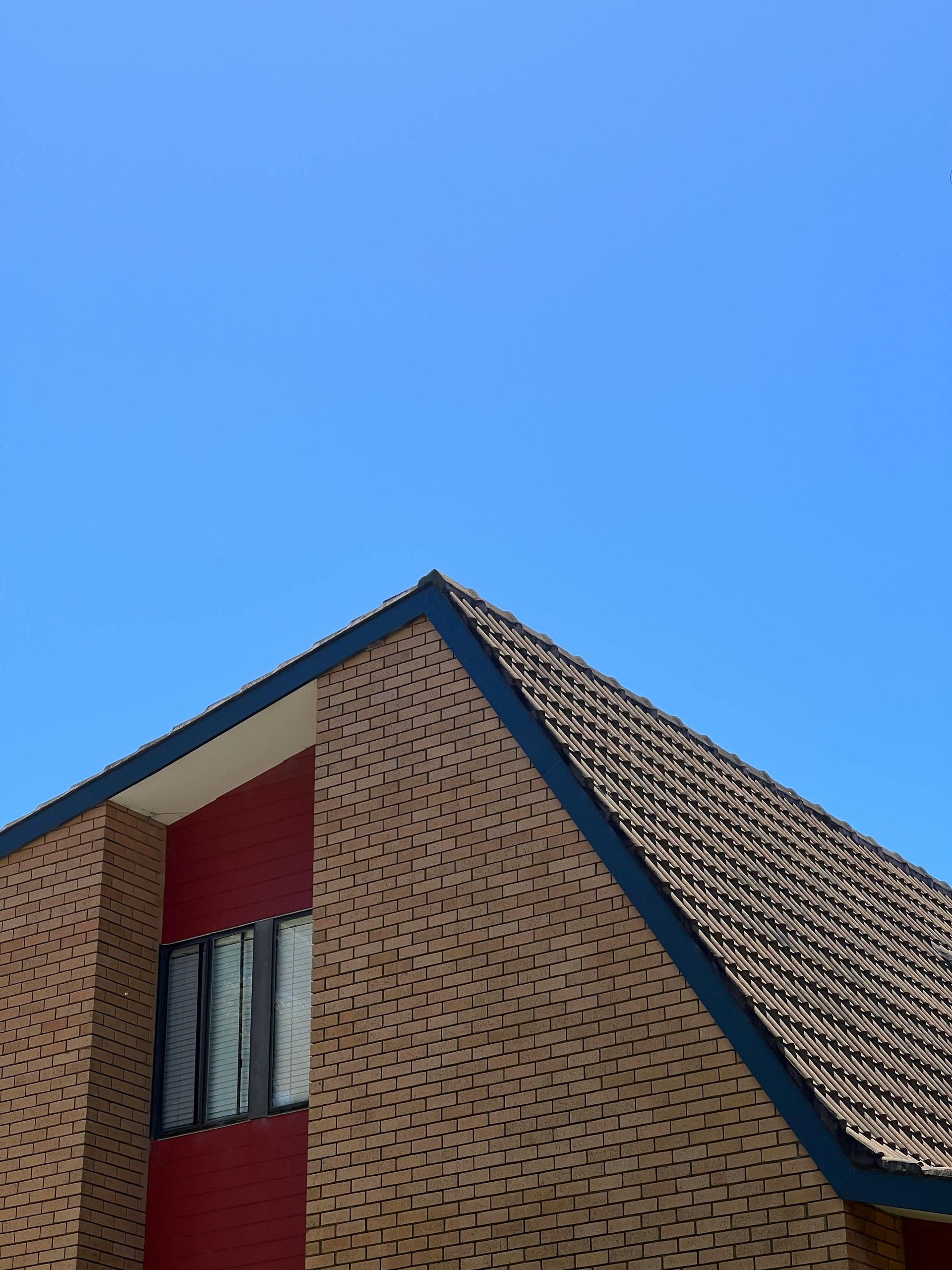 Brick house corner with red wall and blue roof against a clear blue sky