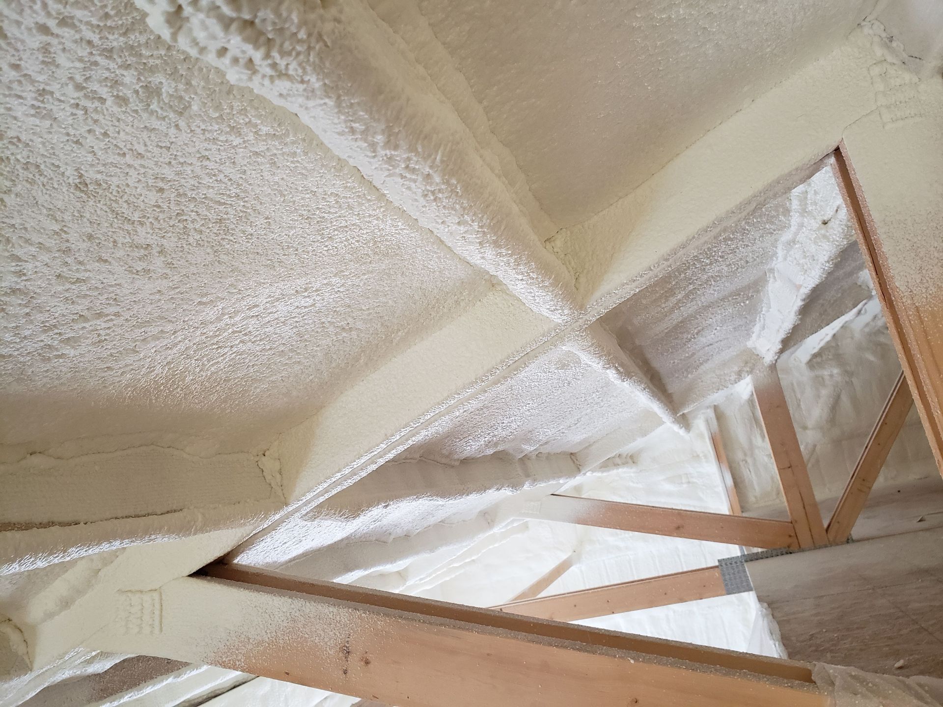 Attic interior with spray foam insulation on rafters and ceiling.  White and light tan colors.