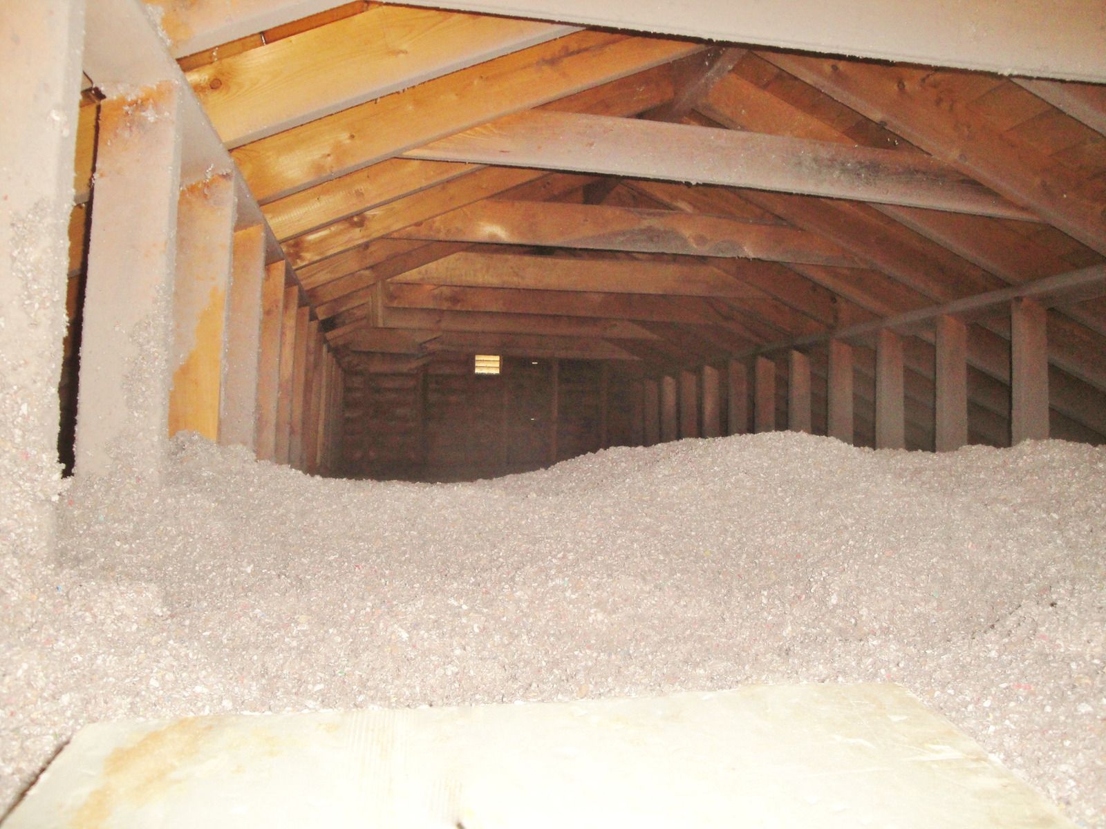 Attic interior filled with loose, light-colored insulation; wooden beams and rafters support the roof.