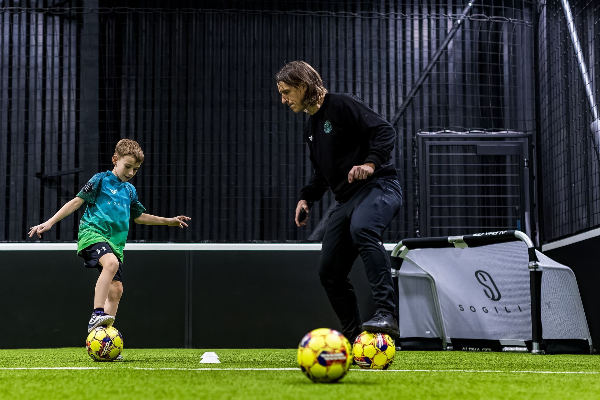 A girl is kicking a soccer ball between two orange cones on a field.