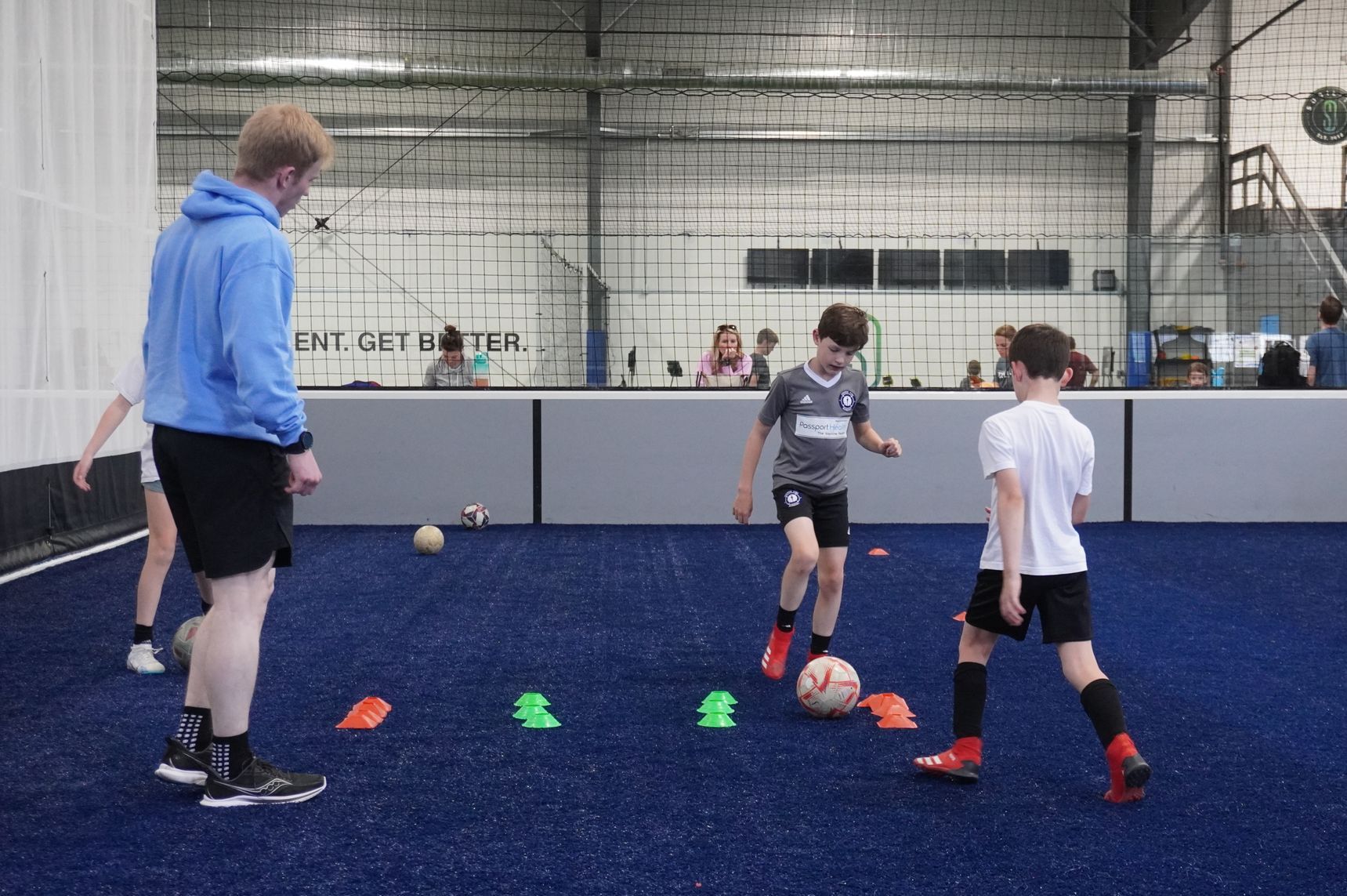 A girl is kicking a soccer ball between two orange cones on a field.