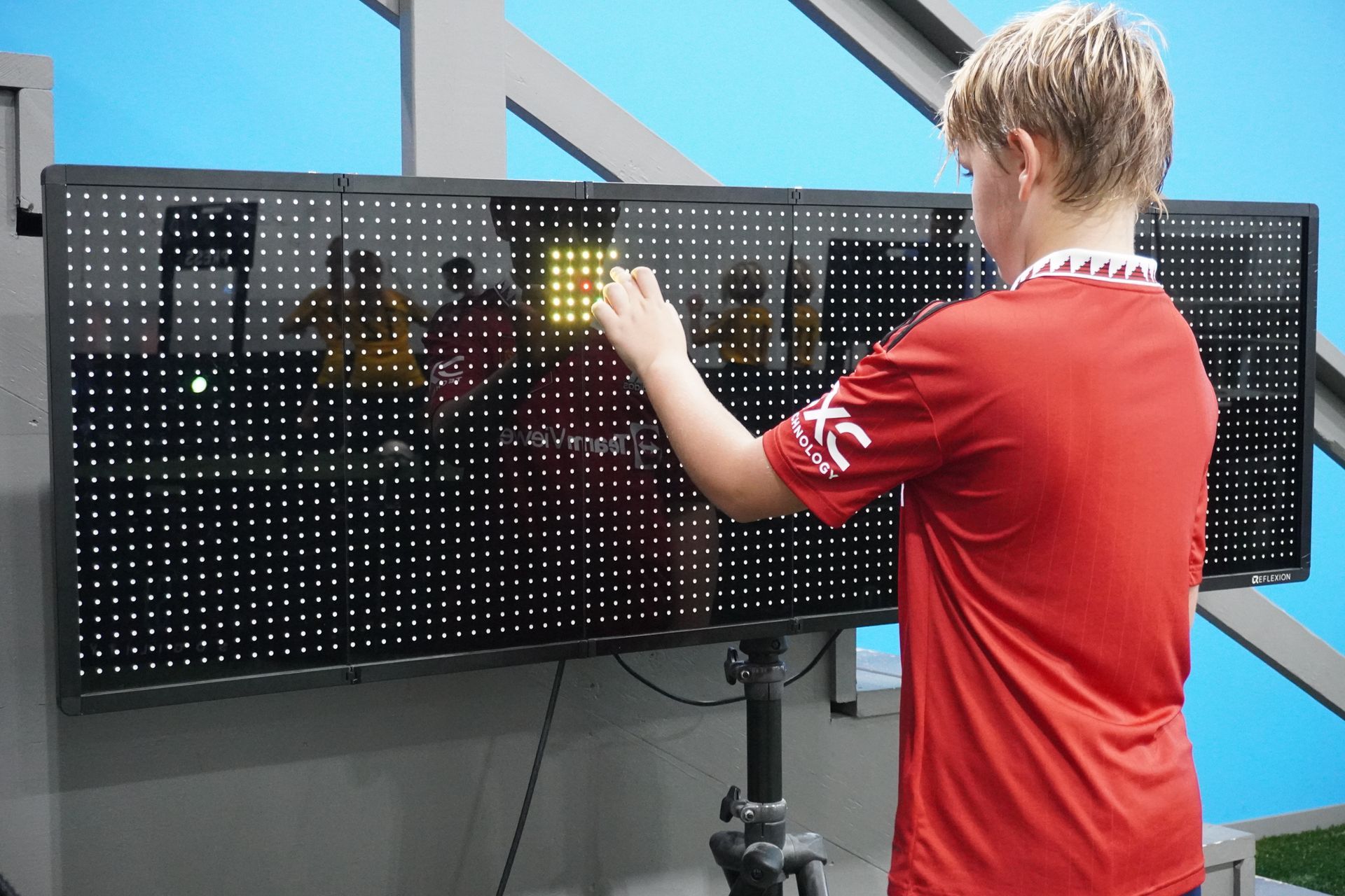 A young boy in a red shirt is standing in front of a scoreboard