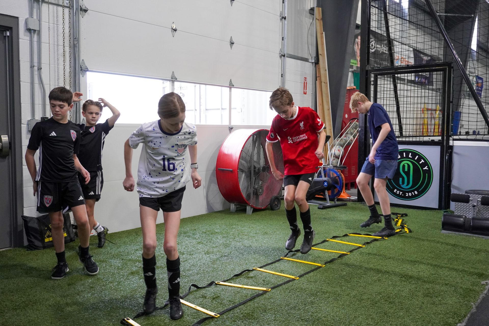 A group of young boys are jumping over a ladder in a gym.