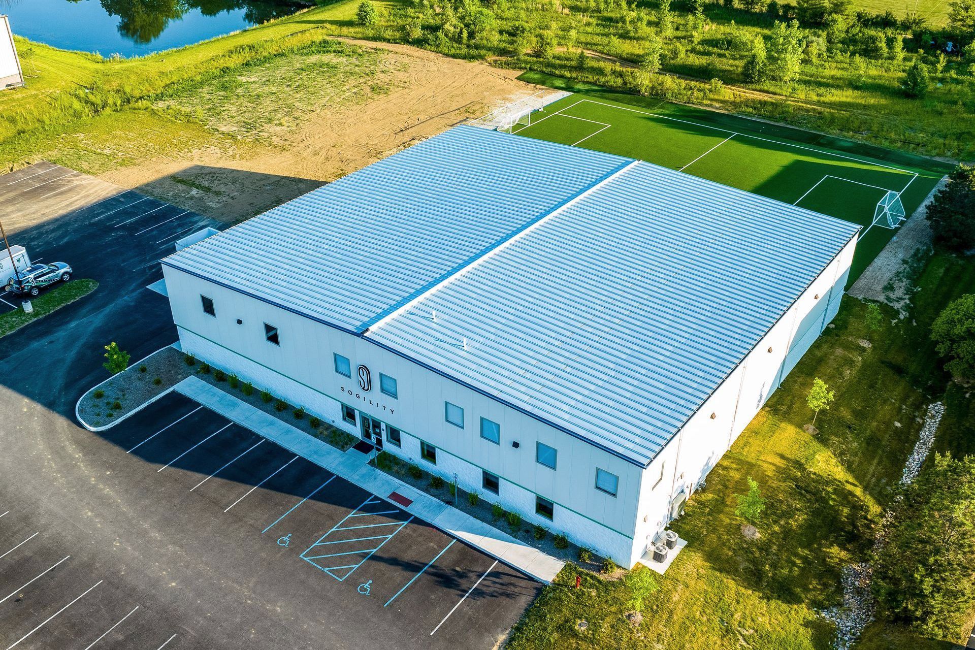 An aerial view of a large white building with a football field in the background.