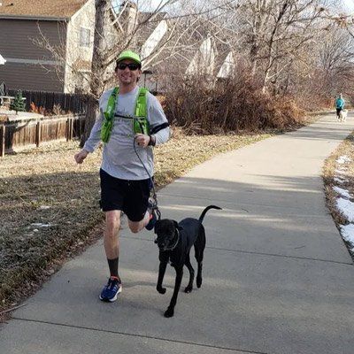A Denver Dog Jogger  is running with a black dog on a leash.
