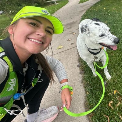 Lindsi smiling with dog on leash and  path, wearing running gear, lime green hat.