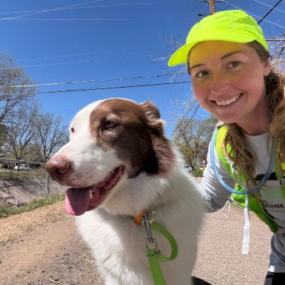 Morgan smiling with dog on leash and  path, wearing running gear, lime green hat.