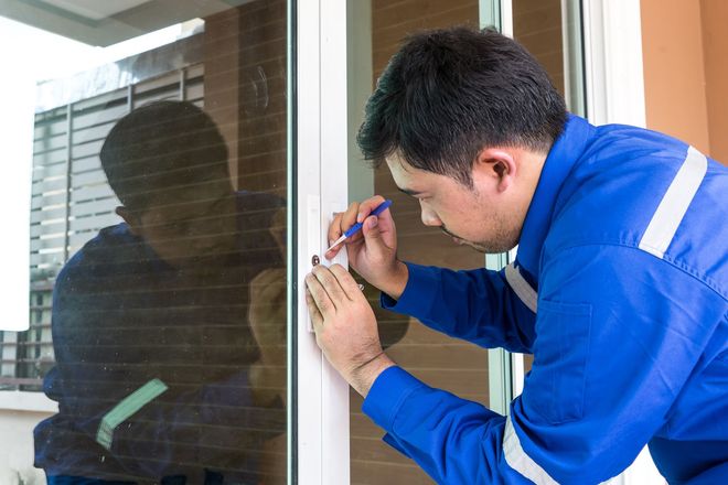 A person in blue overalls repairing a window, using a small tool.