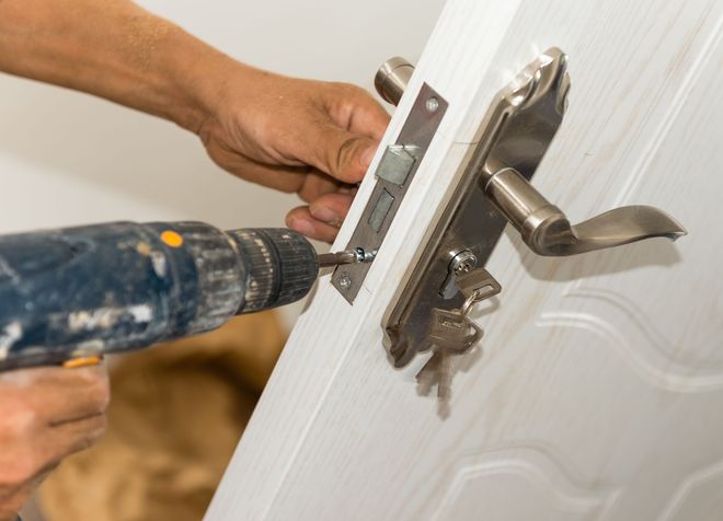 Person using a drill to install a door lock on a white door.