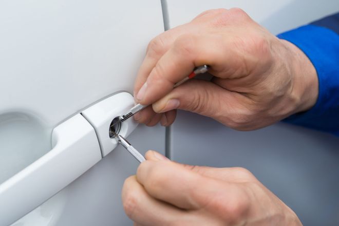 Hands using lock picks to open a white car door lock.