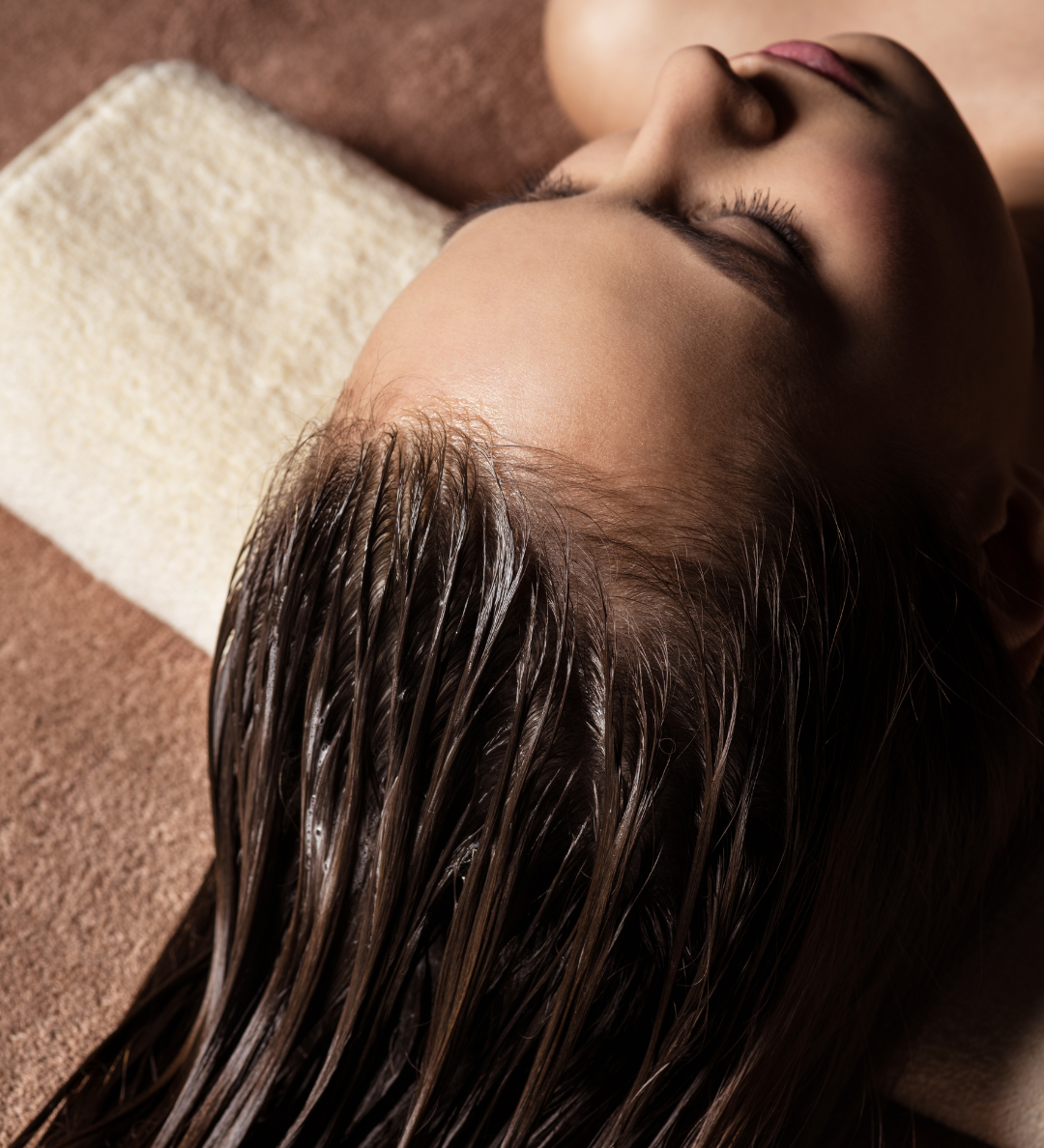 Woman with wet hair lying on a towel, eyes closed.  Brown hair, neutral background.