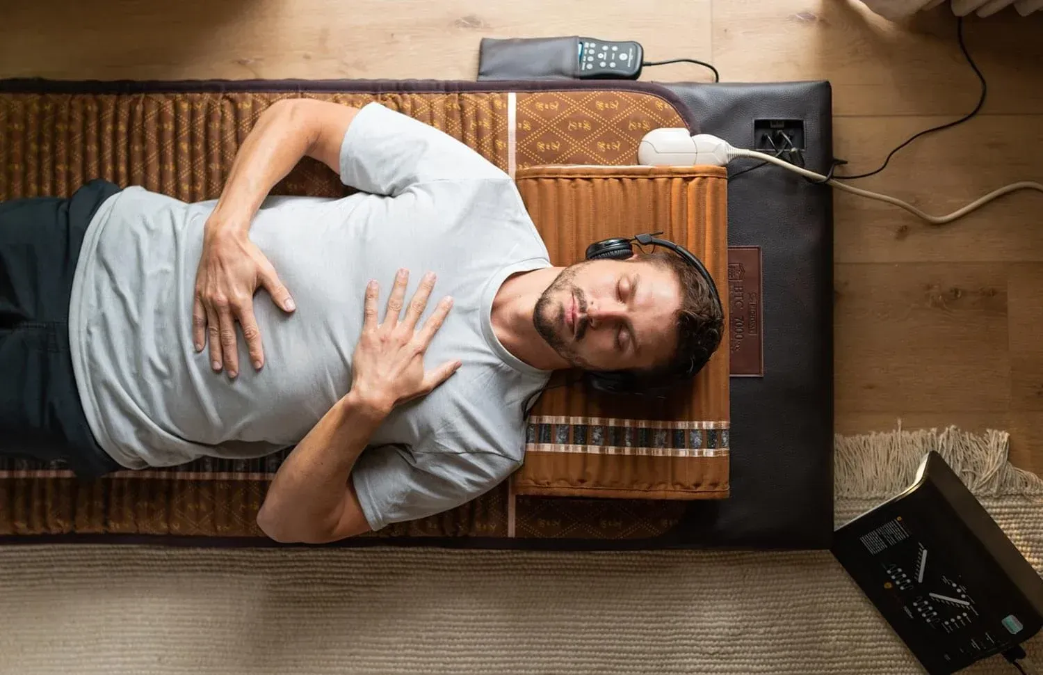A man is laying on a biomat with headphones on relaxing