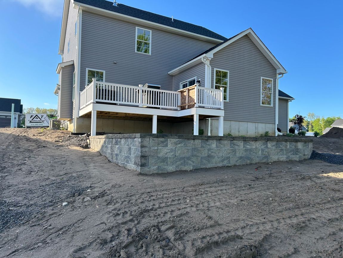 The back of a house with a large deck and a stone wall.