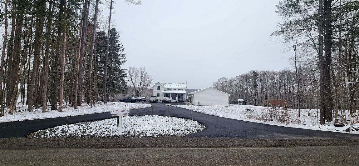 A snowy driveway leading to a house in the woods.