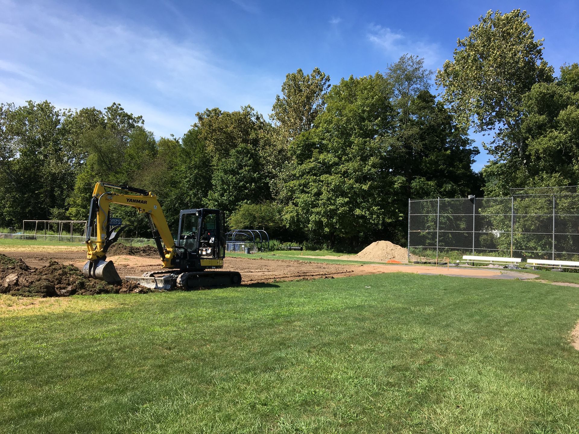 A yellow excavator is digging a hole in a grassy field.