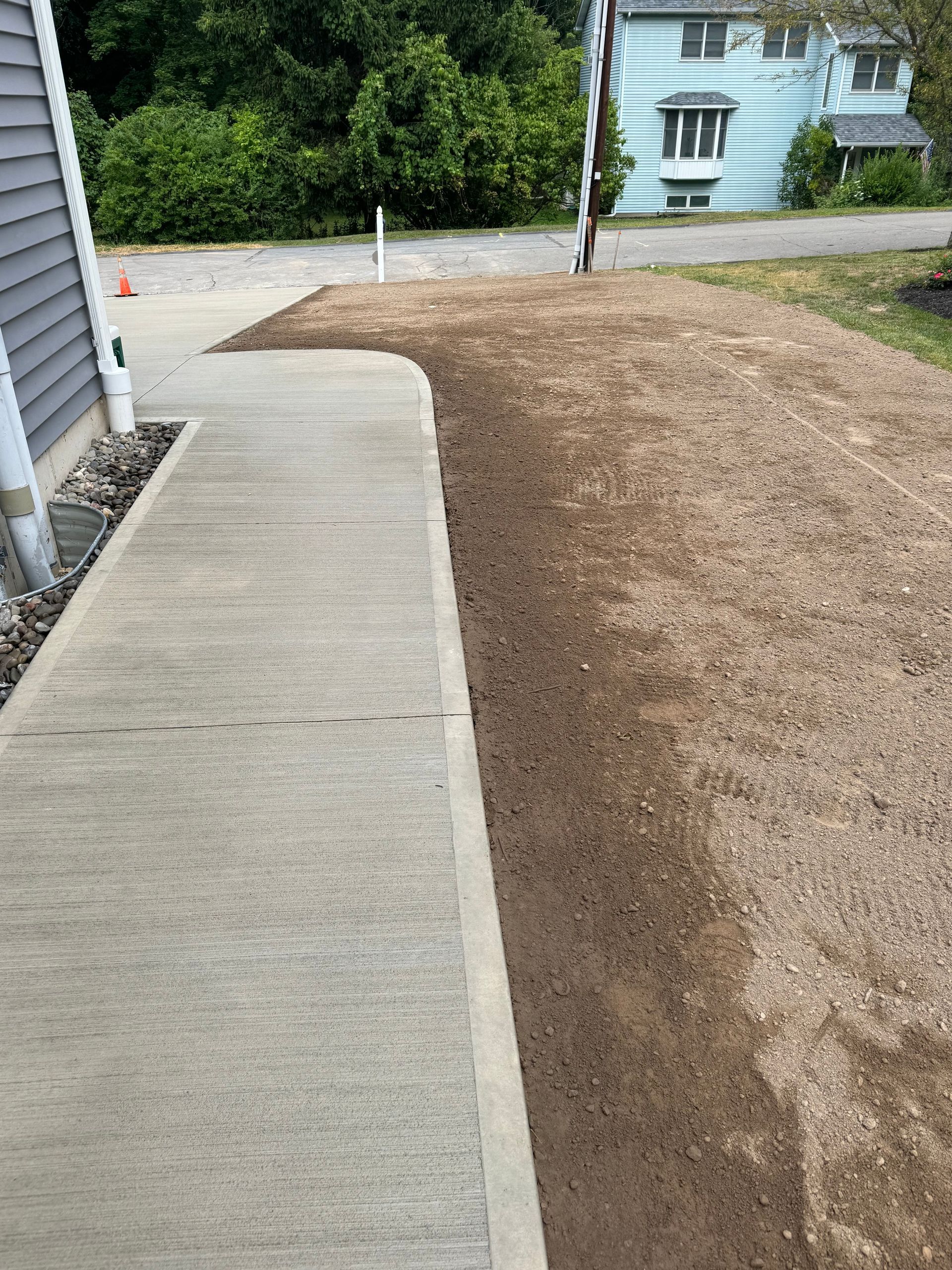 A concrete walkway leading to a house next to a dirt field.