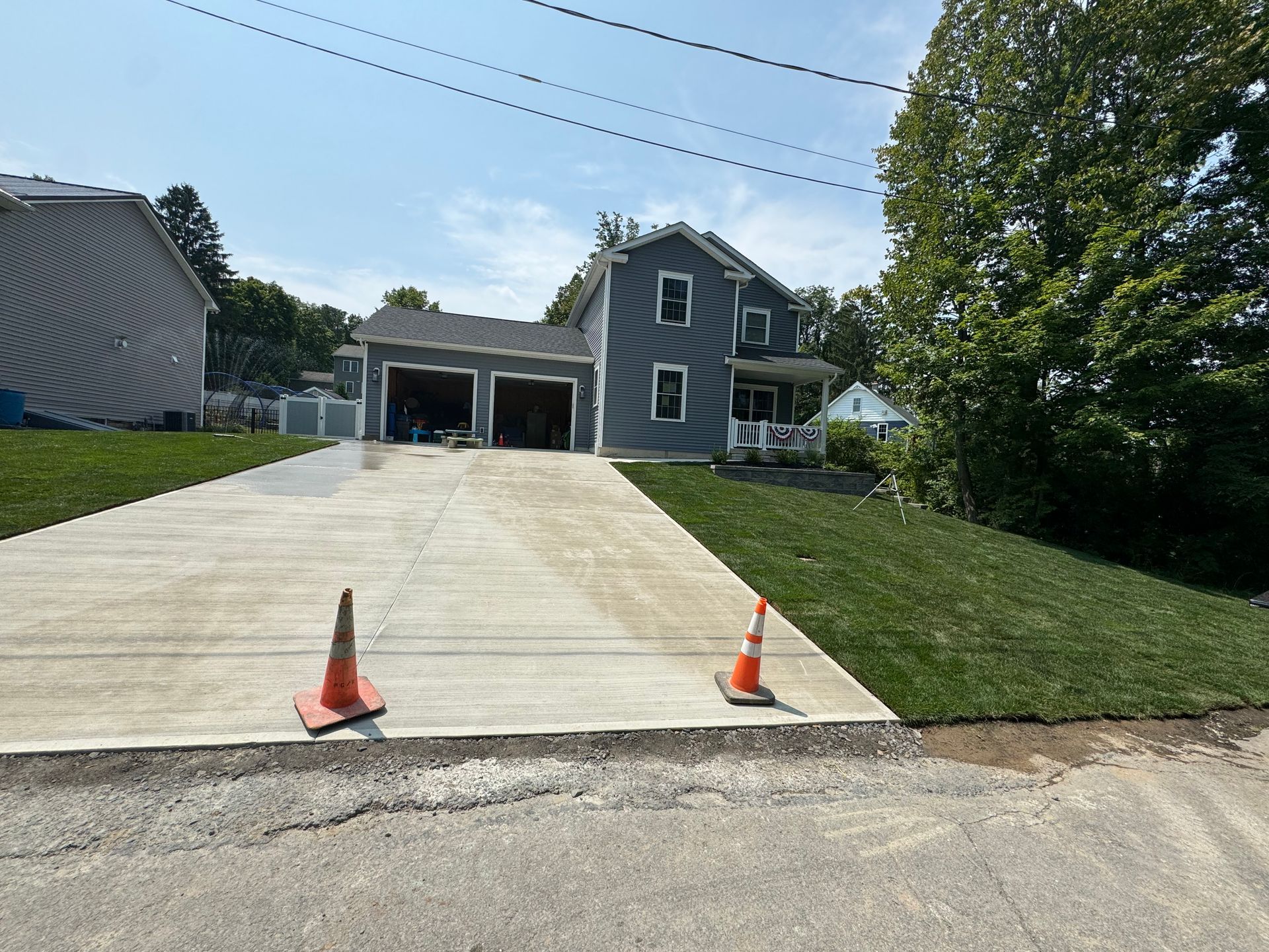 A concrete driveway with two orange cones in front of a house.