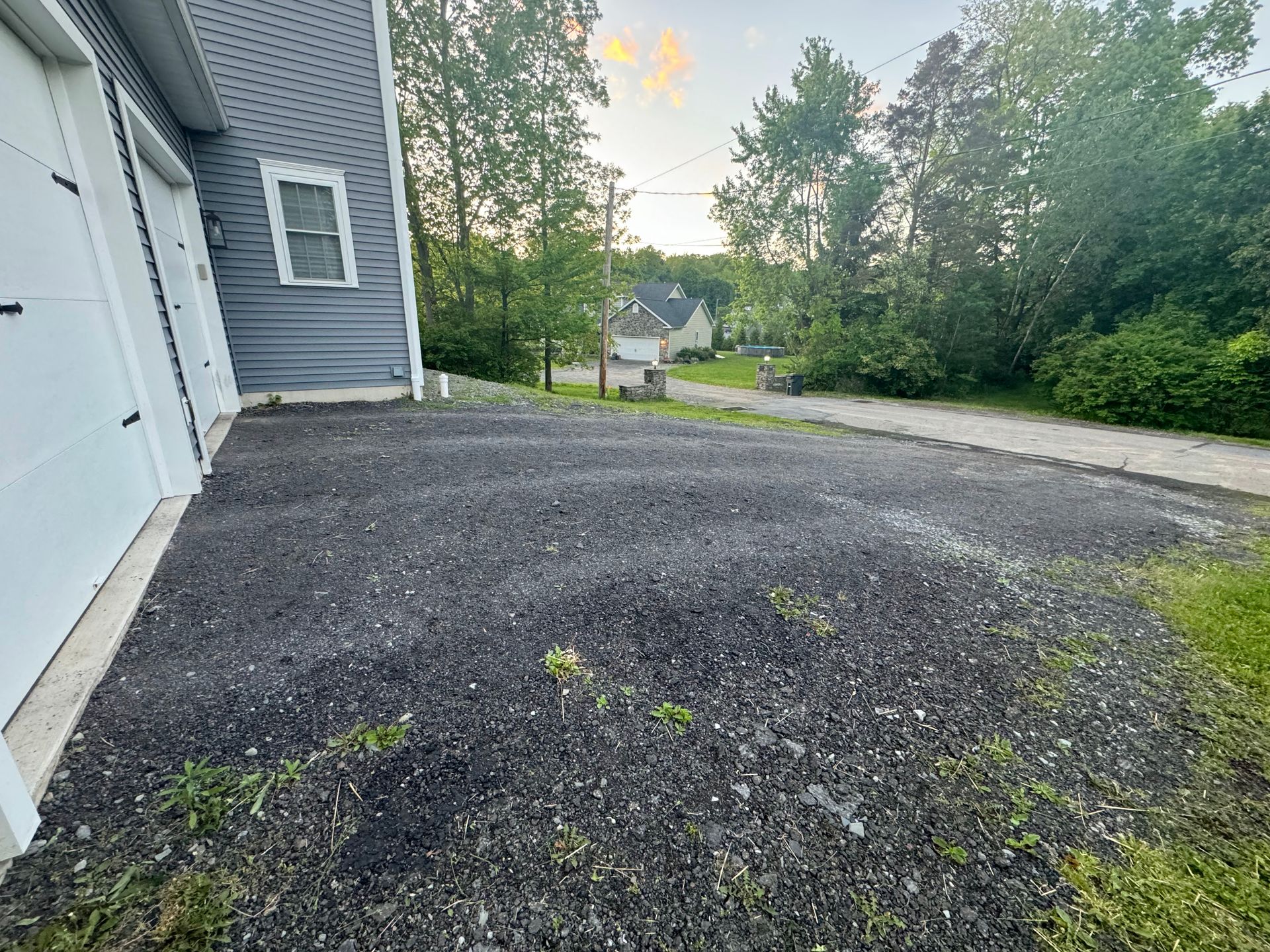 A gravel driveway next to a garage with a house in the background.