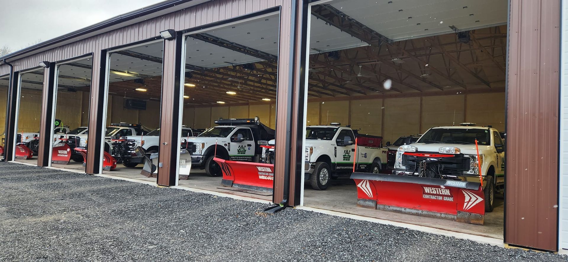 A row of snow plows are parked in a garage.