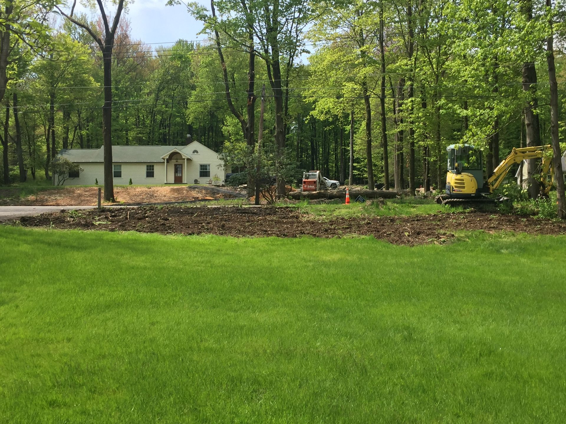 A house is being built in the woods next to a large lush green field.