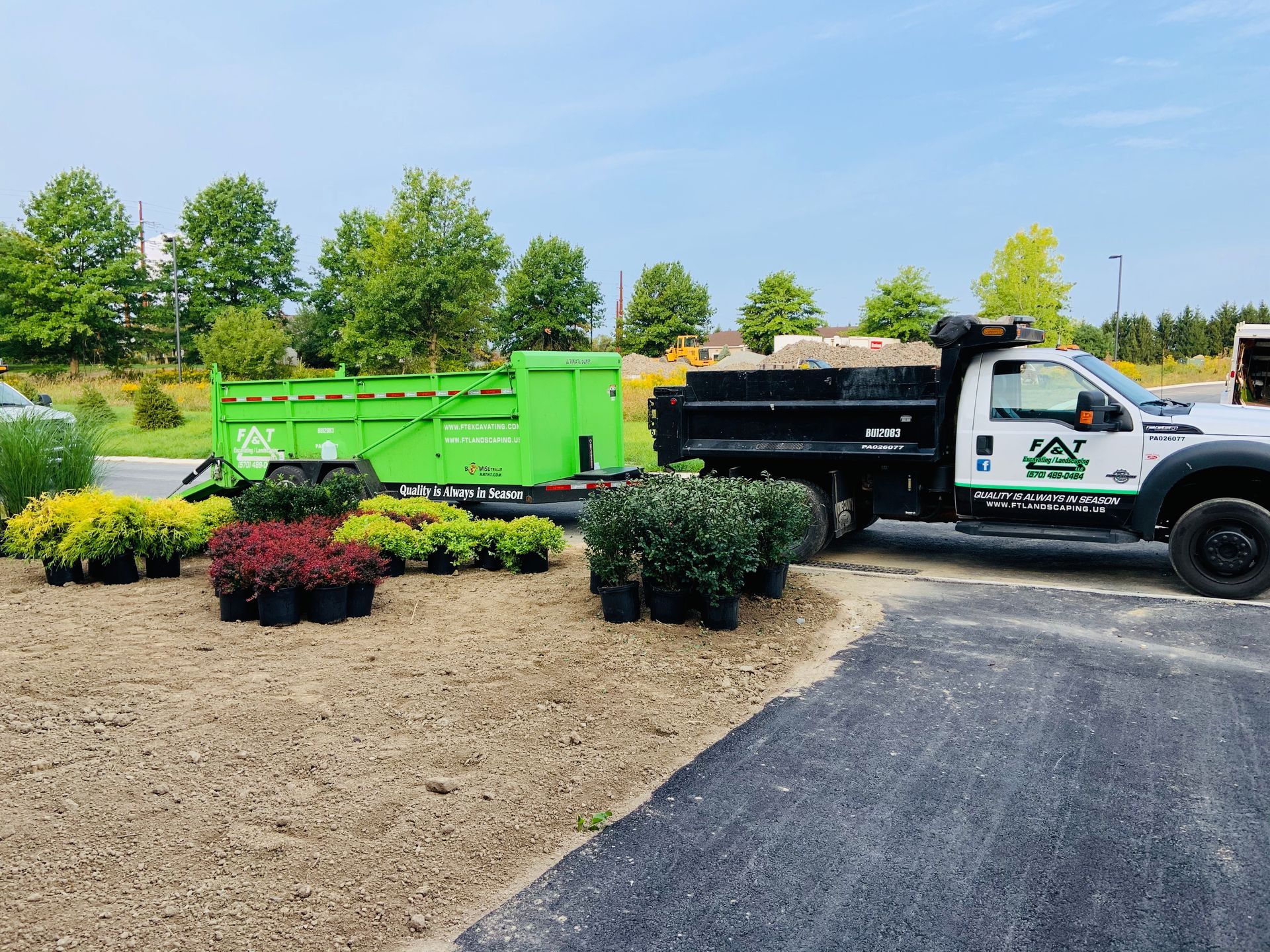 A dump truck is parked next to a trailer filled with potted plants.