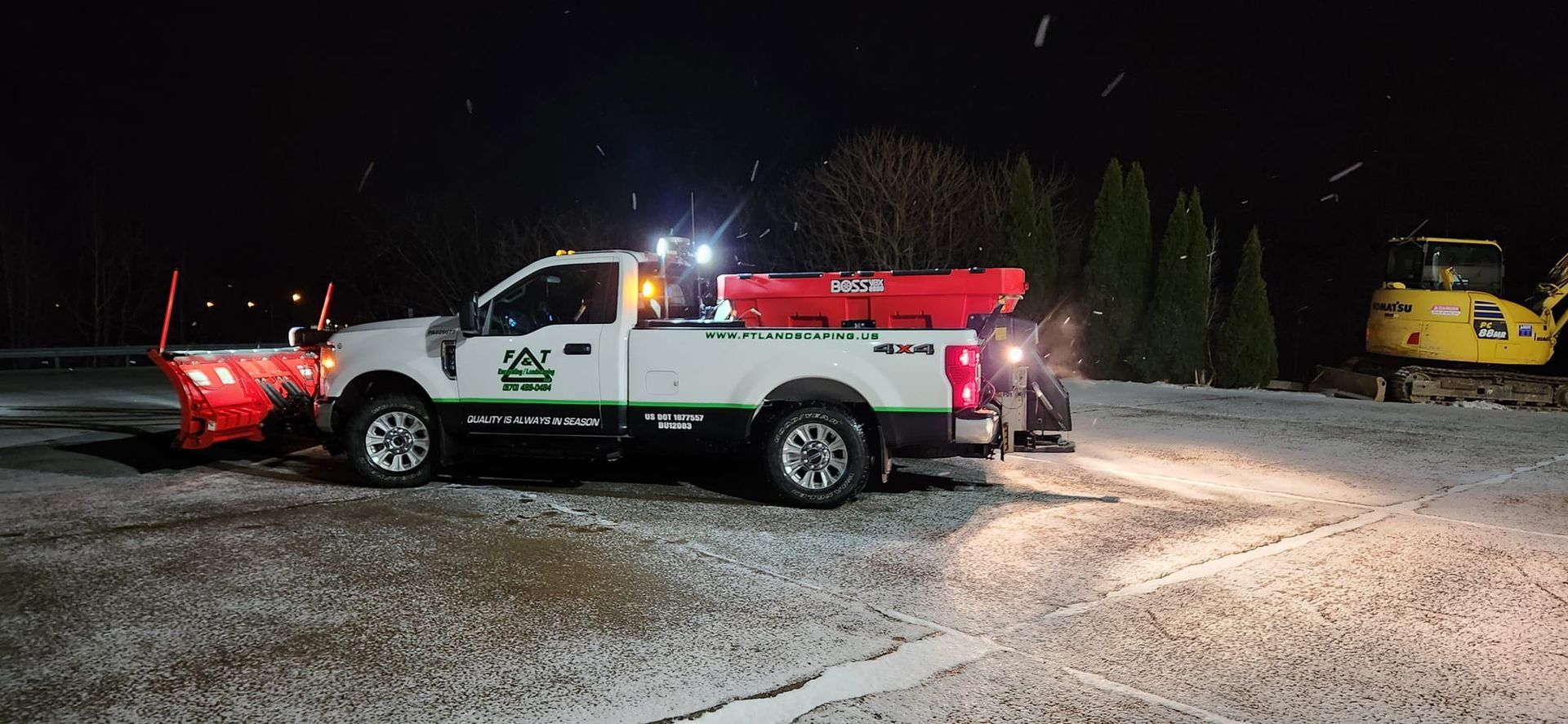 A snow plow is parked in a parking lot at night.