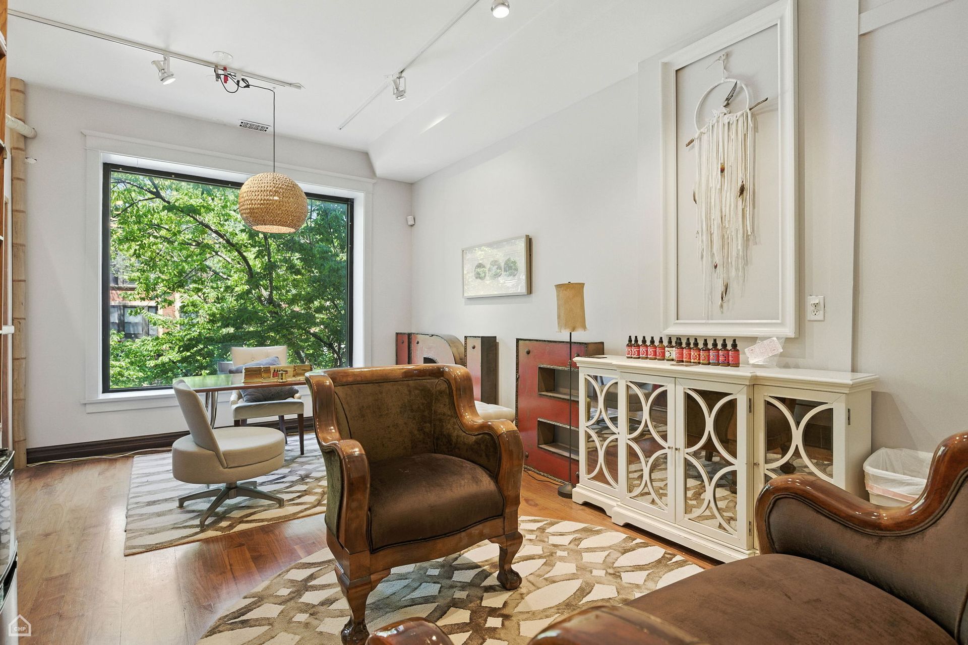 A bright room with a large window, seating, artwork, and white storage cabinet.
