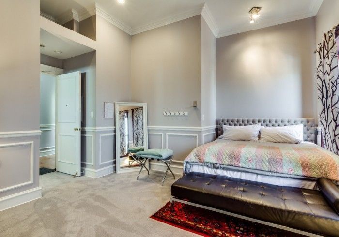 Bedroom with gray walls, bed, mirror, bathroom door, and patterned rug.