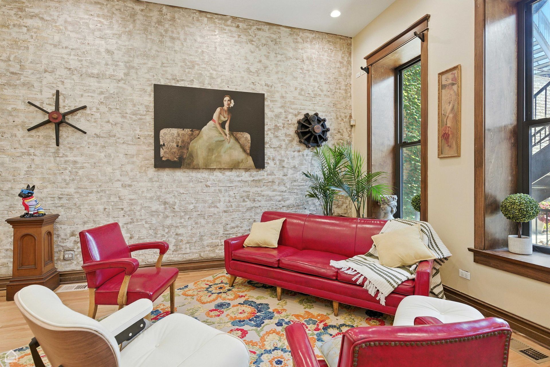 Living room with red sofa, armchairs, artwork, and exposed brick wall.