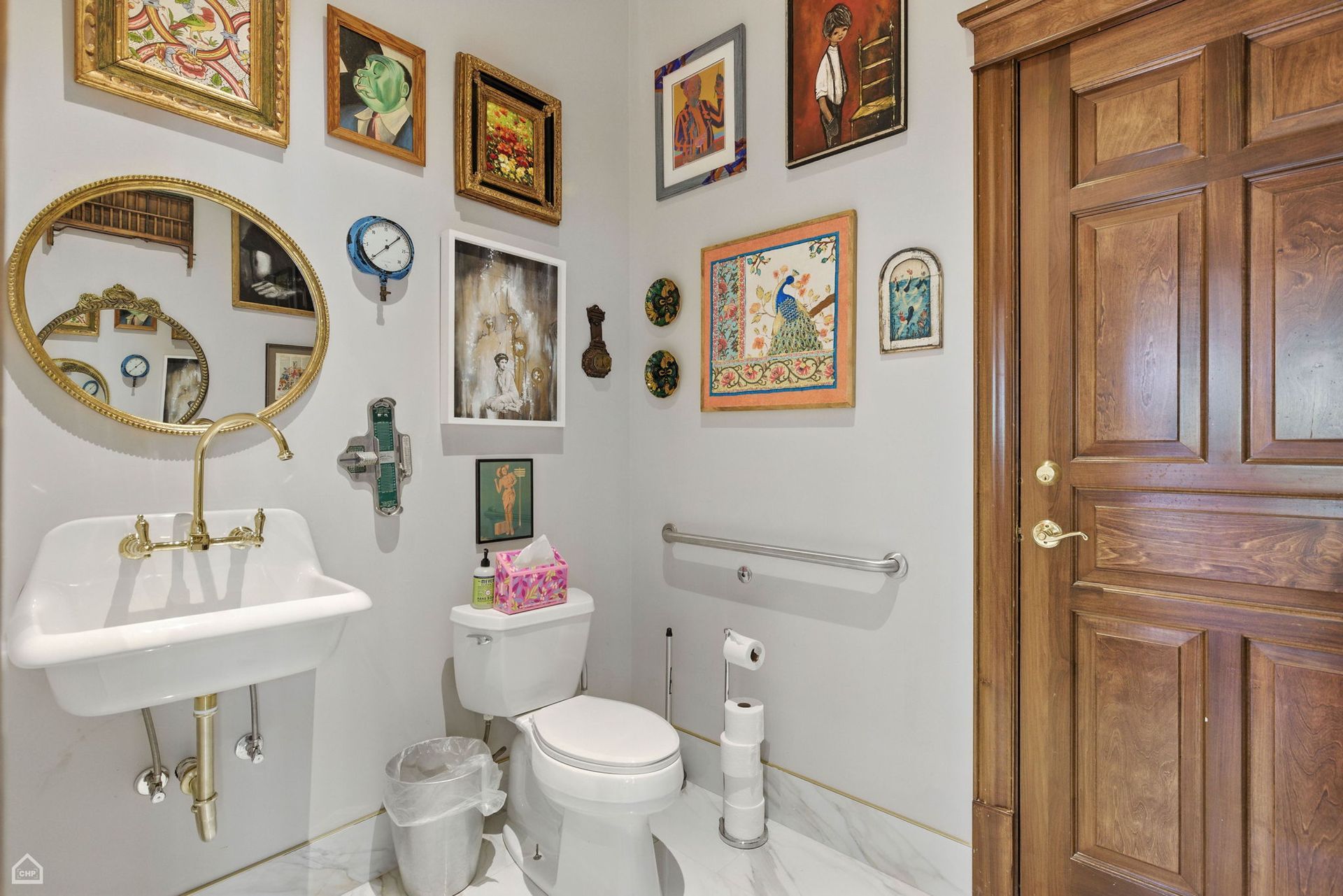 Small bathroom with ornate gold-framed art, antique sink, wooden door, and a white toilet.
