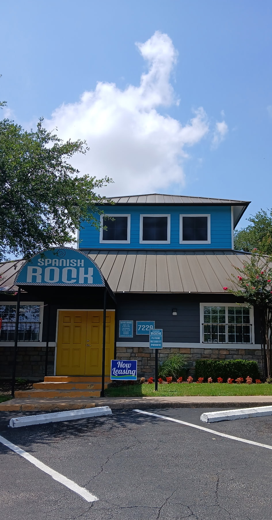 A blue and gray building with a yellow door and a parking lot in front of it.
