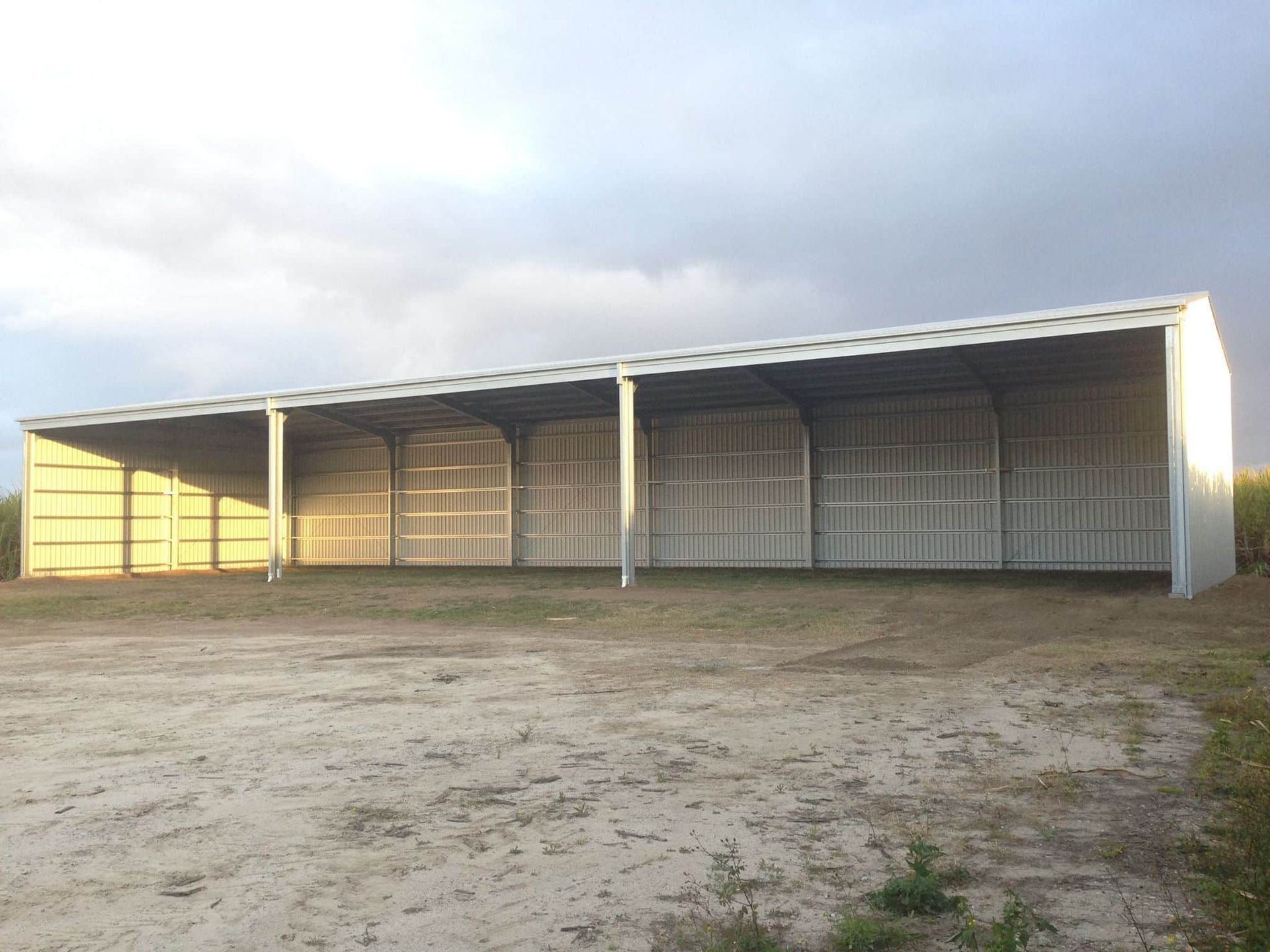 A Large White Building Is Sitting In The Middle Of A Dirt Field — Austeel Sheds in Collinsville, QLD