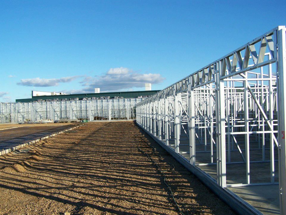 A Row Of Metal Frames Along A Dirt Road With A Building In The Background — Austeel Sheds in Bowen, QLD