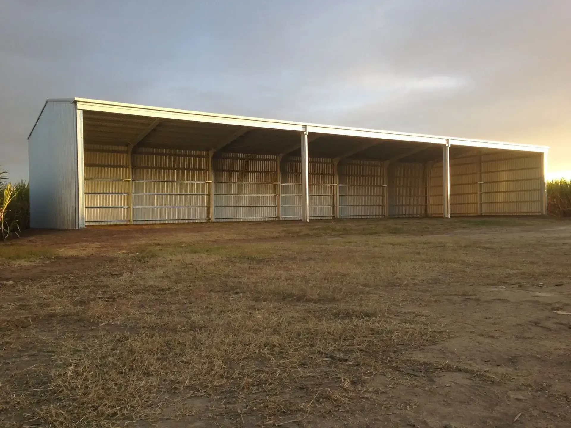 A Large Metal Building Is Sitting In The Middle Of A Dirt Field — Austeel Sheds in Bowen, QLD