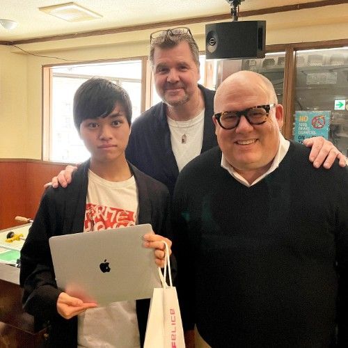 Three men are posing for a picture while one of them is holding an apple tablet.