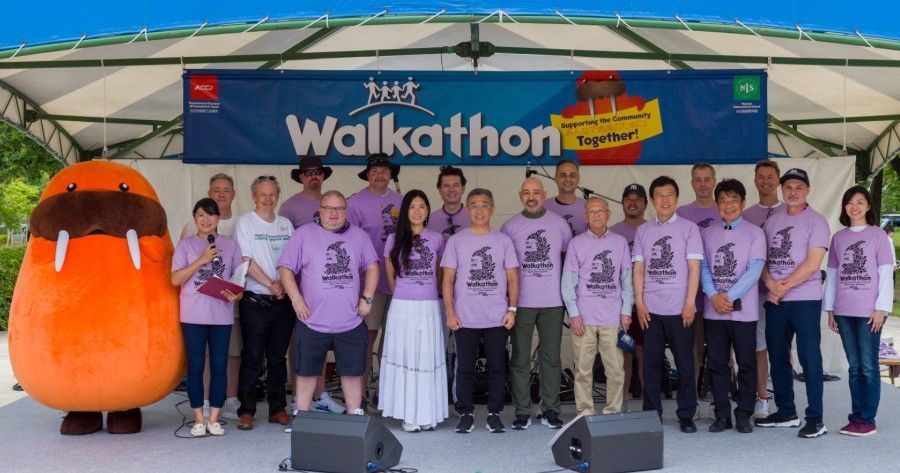 Group of people in matching purple shirts on a stage at a Walkathon event with a large orange mascot