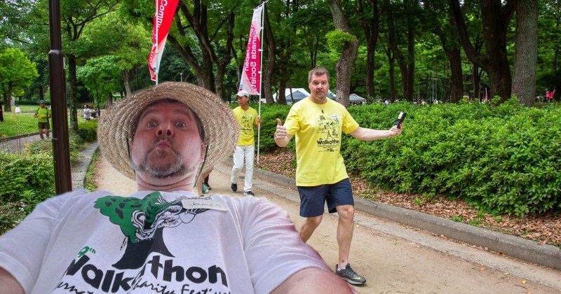 A man wearing a straw hat is taking a selfie in a park.
