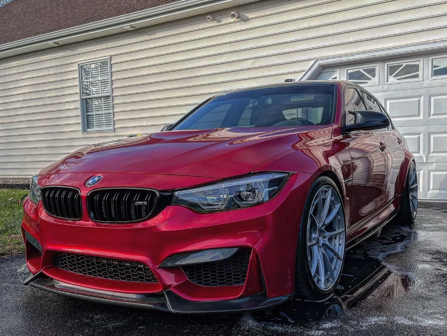 A red bmw m3 is parked in front of a garage door.