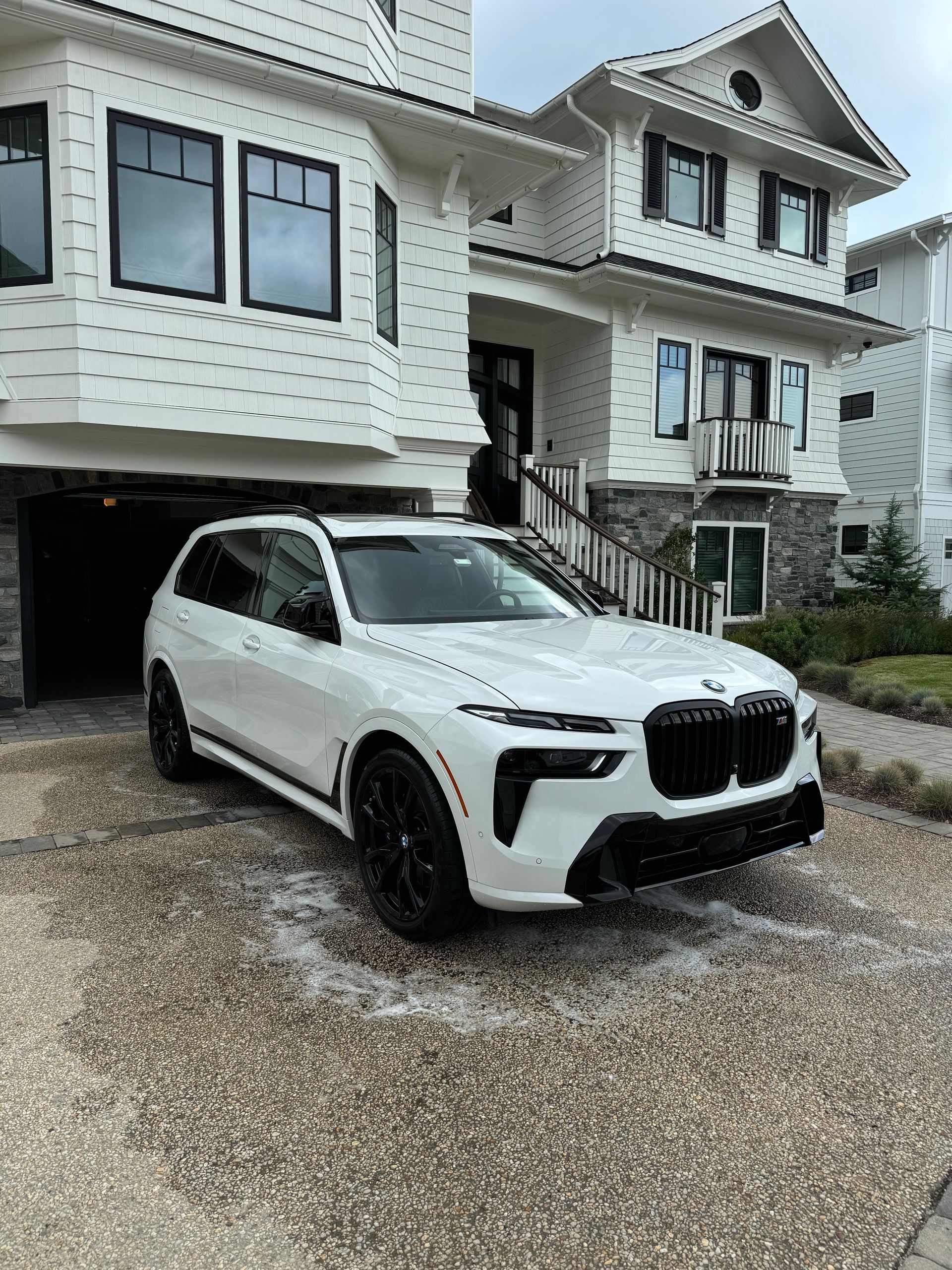 A white bmw x7 is parked in front of a large white house.
