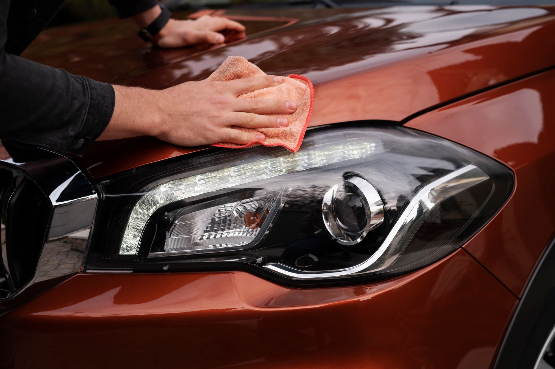 A person is cleaning the headlight of a car with a cloth.